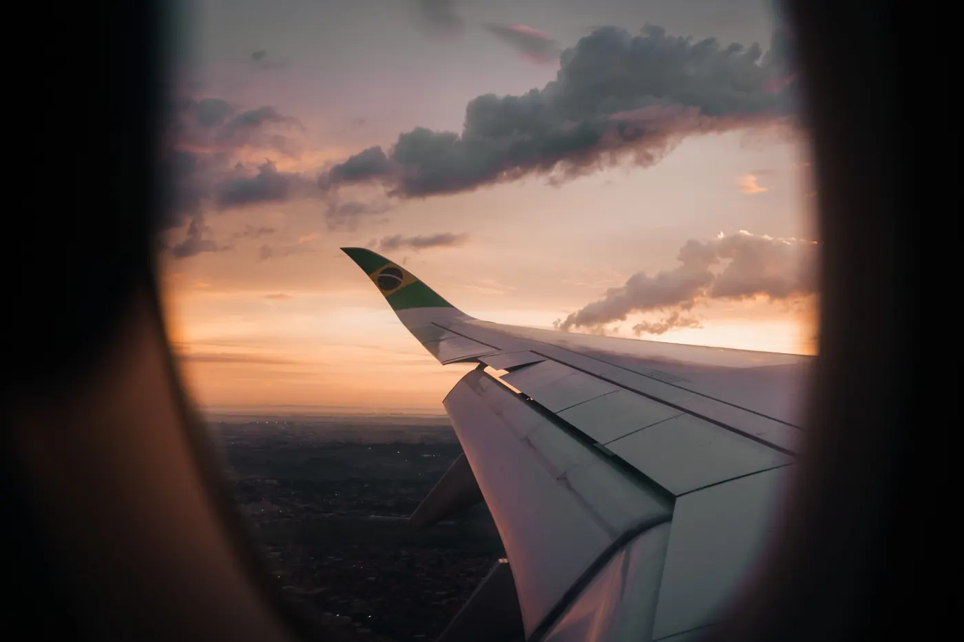 Asa de um avião com a bandeira do Brasil na ponta, vista da janela ao entardecer